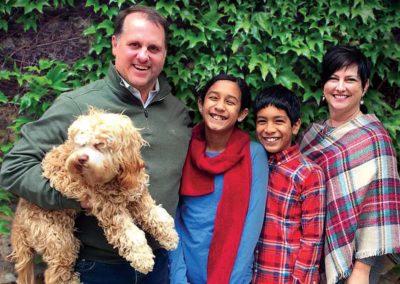 A family of four standing in front of an ivy wall while the dad holds a dog